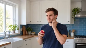 Hand holding an apple with a single bite taken out, representing tooth pain triggered by chewing
