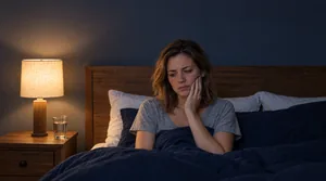 Person sitting up in bed at night with a thoughtful expression while dealing with tooth pain